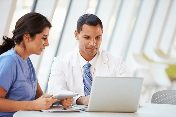 Two doctors in medical residency working next to each other while looking at a laptop. 