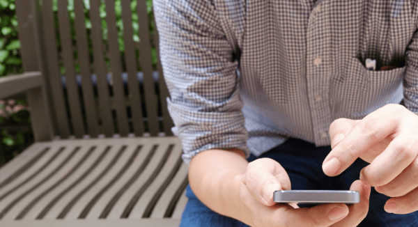 man sitting on bench typing a number into his phone 