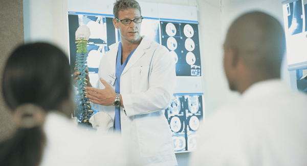 doctor pointing to spine in front of screen of xrays